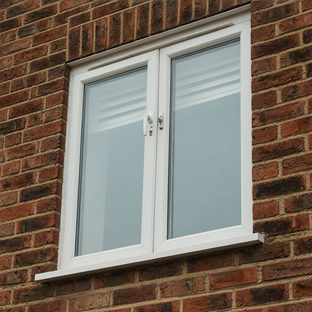 Close-up van een wit kunststof kozijn met ingebouwd ventilatierooster en espagnoletslot